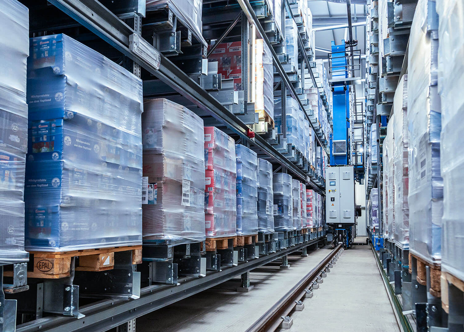 Gang im Kompaktlager von System Logistics mit Paletten an den Seiten und fahrerlosem Fahrzeug auf Schiene