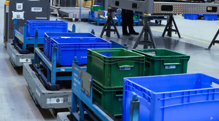 Transportzug von System Logistics in Produktionshalle der Industrie transportiert mehrere Kisten auf W&auml;gen