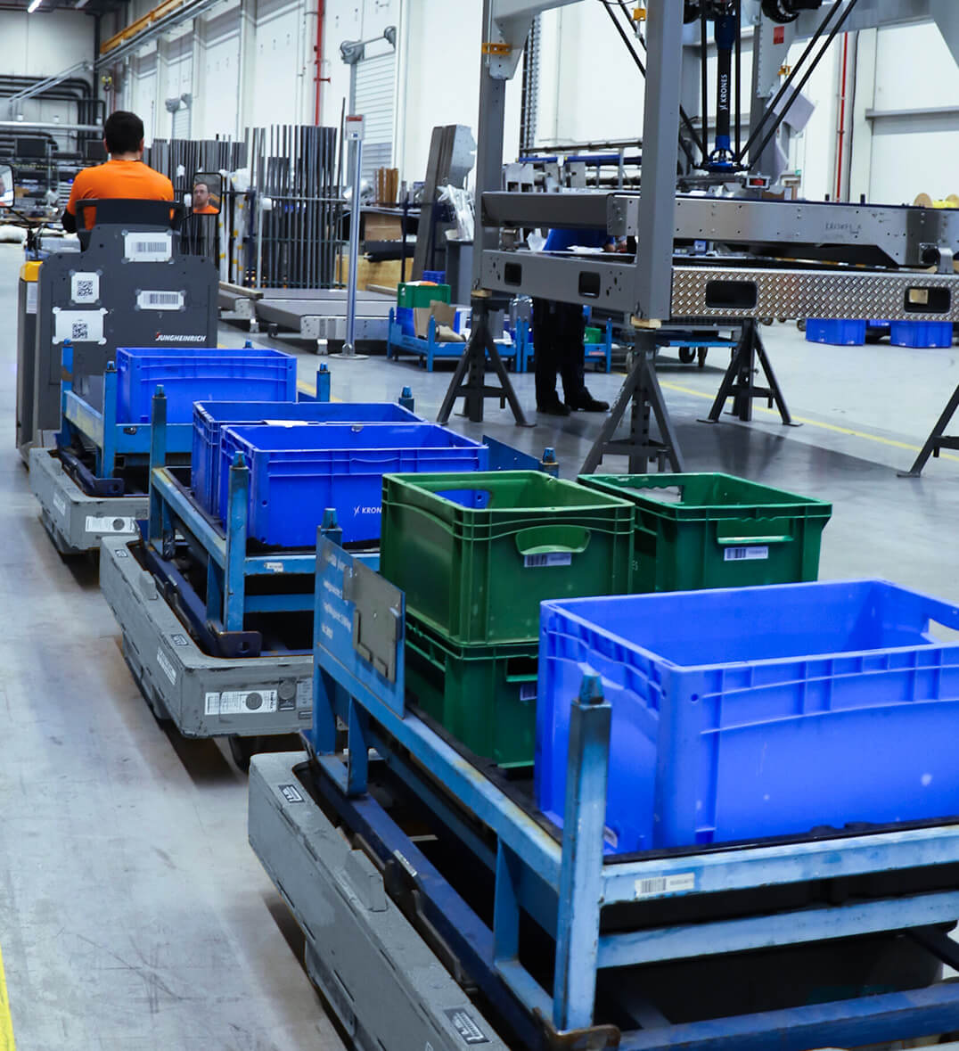 Transportzug von System Logistics in Produktionshalle der Industrie transportiert mehrere Kisten auf W&auml;gen